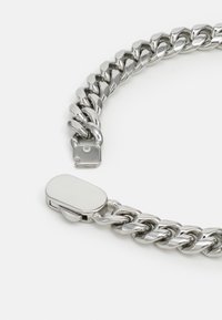 Bracelet en métal argenté composé de maillons ovales et ronds entrelacés, avec un fermoir rectangulaire lisse. Finition polie.