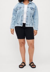 Vaaleansininen farkkutakki, jossa on etutaskut, valkoinen t-paita, mustat istuvat shortsit ja mustat sandaalit hihnoilla ja koristeellisella soljella.