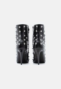 Čierne kožené členkové topánky s vysokými ihličkovými podpätkami, zdobené okrúhlymi striebornými cvočkami rozmiestnenými po vonkajšom povrchu.