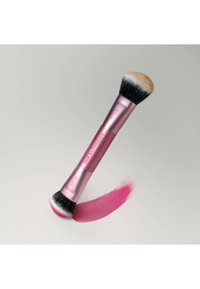Pinceau de maquillage Real Techniques à double embout rose avec des poils blancs et noirs appliquant un échantillon de produit cosmétique rose.
