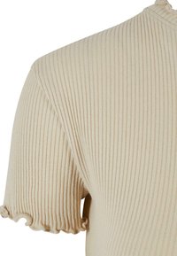 Haut en tricot beige à fines côtes avec des manches courtes et des ourlets en formes de vagues, présentant une coupe ajustée et une texture douce dans l'ensemble.