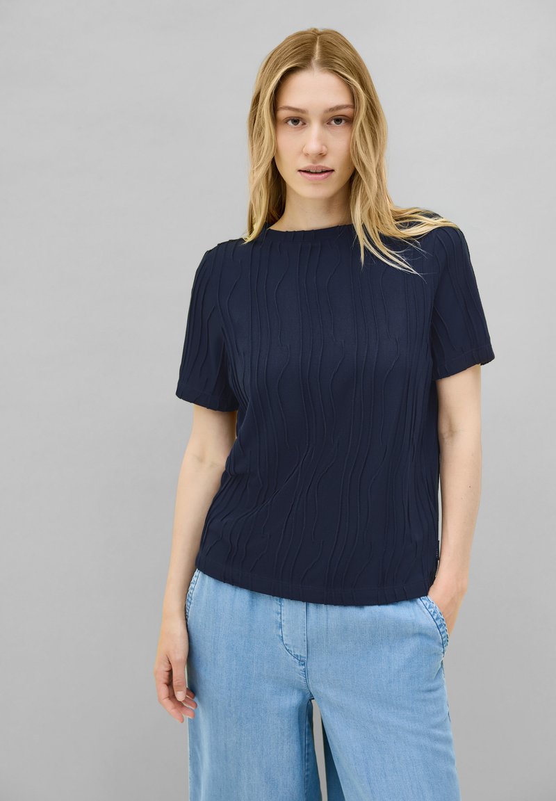 Blusa de manga corta en color navy con patrón texturizado de olas, escote redondo y corte holgado, combinada con pantalones anchos de un azul claro.