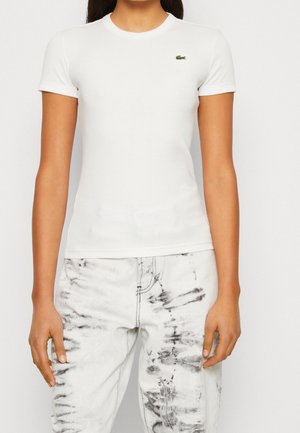 Biały prążkowany T-shirt z krótkim rękawem i okrągłym dekoltem. Posiada małe zielone logo krokodyla na lewej piersi.