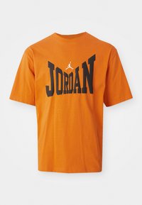Orange bomulds-T-shirt med stort sort "JORDAN" tekst og et lille hvidt Jumpman-logo over teksten. Kortærmet og design med rund hals.