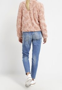 Różowa, teksturowana, puszysta kurtka z falistym wzorem, dobrana z jasnoniebieskimi, dopasowanymi dżinsami oraz białymi trampkami, widziana z tyłu.