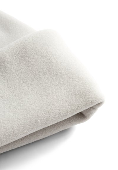 Gros plan d'un tissu polaire doux, gris clair, plié sur un fond blanc, montrant sa surface texturée et moelleuse.