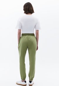 Joggers verdes con cintura elástica presentan un diseño cónico con puños en los tobillos, combinados con una camiseta blanca de corte corto.