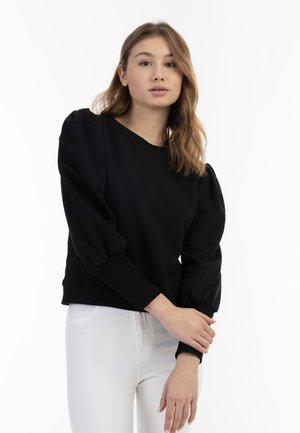 Zwarte cropped sweatshirt met poffende mouwen, ronde halslijn en geribbelde manchetten, gecombineerd met witte slim fit jeans. Glad textuur, minimalistisch ontwerp.