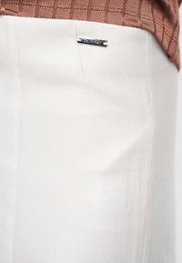 Κοντινή λήψη λευκών παντελονιών Calvin Klein με καφέ πλεκτό πουλόβερ που φαίνεται στη μέση.