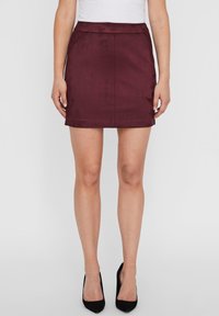 Saia mini burgundy com textura suave, design ajustado e uma bainha limpa. Estilizada com uma blusa branca e sapatos de salto preto de bico fino.