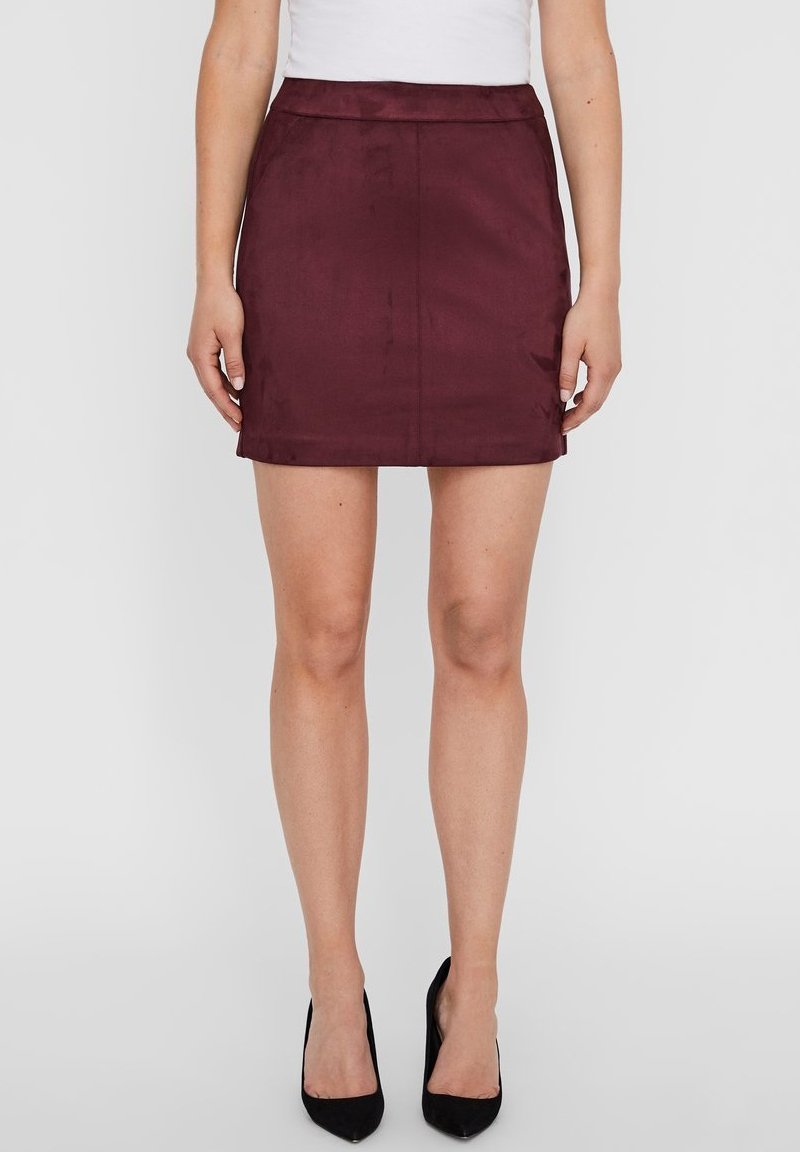 Saia mini burgundy com textura suave, design ajustado e uma bainha limpa. Estilizada com uma blusa branca e sapatos de salto preto de bico fino.