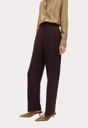 Femme portant un pantalon large marron foncé taille haute, un chemisier à rayures beige avec boutons, et des mules beige à talons petits et pointus.