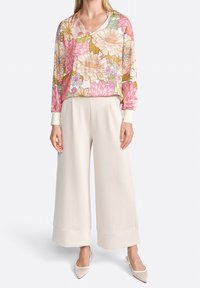 Blusa de mangas largas con estampado floral en rosa, amarillo y verde; combinada con pantalones de pierna ancha en color crema; modelo llevando zapatos de tacón puntiagudos en tonos neutros.