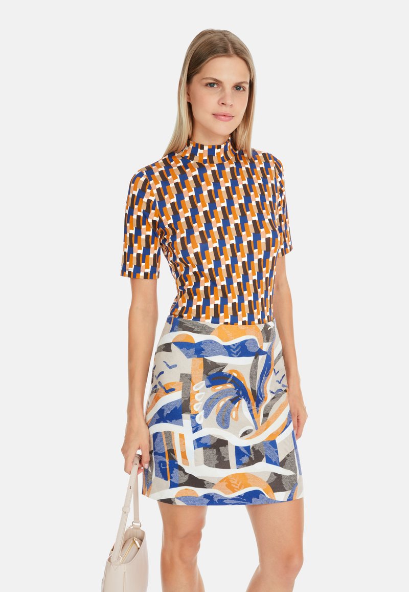 T-Shirt mit kurzen Ärmeln und geometrischem Muster in Orange, Blau und Braun; kombiniert mit einem gemusterten Rock, der abstrakte Designs in Blau, Orange und Grau aufweist.