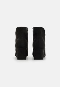 Botines de ante negro con tacón cuadrado, que presentan una cremallera lateral y una textura suave, diseñados para un ajuste ceñido.