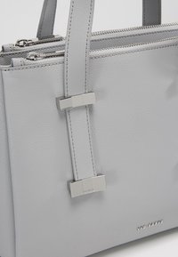 Sac à main en cuir texturé gris clair avec double compartiments zippés et ferrures argentées sur les anses et le coin inférieur avant.