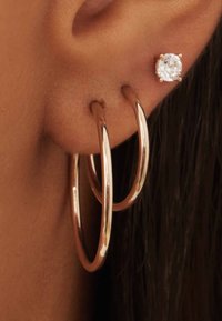 Roze gouden hoepeloorringen met een glanzende afwerking, gecombineerd met een kleine ronde cubic zirconia studs. Close-up van het oor.