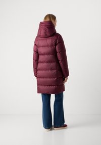 Bordeauxkleurige pufferjas met een capuchon, met een gequilt ontwerp en elastische mouwen. Draagt over flaired jeans, met een gladde, glanzende textuur.