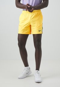 Gula träningsshorts med svarta detaljer, som har resårmidja, två framfickor och en Nike-logotyp på vänster sida.