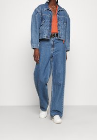 Jeansjacka med avslappnad passform, ljusblå färg och två bröstfickor. Kombinerad med vida blå jeans och vita sneakers.