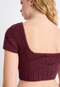 Sweater cropped bordeaux com mangas curtas e decote largo, apresentando um tecido texturizado e barra inferior canelada. Detalhes de costura são visíveis.