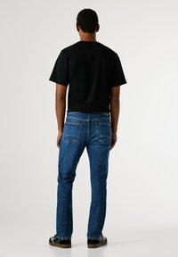 Černé tričko s krátkým rukávem spárované s modrými džíny. Džíny mají pět kapes a běžný střih, s vybledlým vzhledem a detaily šití.