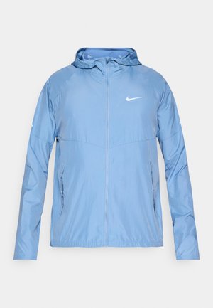 Vaaleansininen Nike-takki hupulla, edessä täysi vetoketju, sivutaskut ja valkoinen logo. Sileä, kevyt kangas ja rento istuvuus.