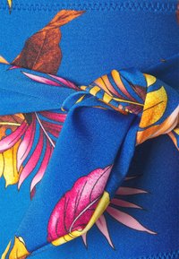 Vestuário azul com um vibrante padrão floral com detalhes em rosa e amarelo; inclui um detalhe de nó atado, feito de um material suave e elástico.