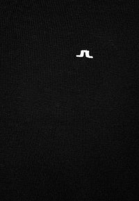 Tessuto a maglia nero con una finitura texturizzata, caratterizzato da un piccolo logo bianco ben visibile al centro.