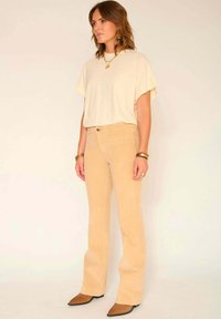 Pantalons en velours côtelé beige clair évasés avec une finition texturée, associés à un haut ample crème, portés avec des ballerines marron à bout pointu.