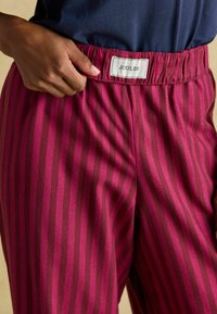 Pantalóny s širokými nohavicami v magentovej a tmavo ružovej pruhovanej kombinácii, s elastickým pásom a viditeľnou etiketou "JOULES" vpredu.