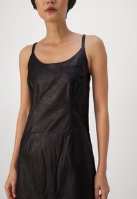 Schwarzes Kunstlederkleid mit dünnen Trägern, zwei Fronttaschen, einer taillierten Silhouette und einer subtil strukturierten Oberfläche.