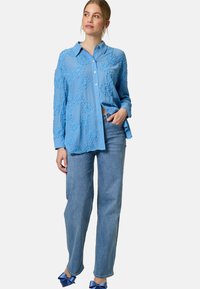 Light blue button-up shirt with textured floral appliqués, paired with light blue straight-leg jeans and blue bow-accented shoes.