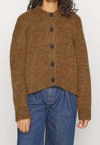 Brun stickad cardigan med rund hals, prydd med stora svarta knappar och en cropped design. Texturerad, varm garn med långa ärmar.