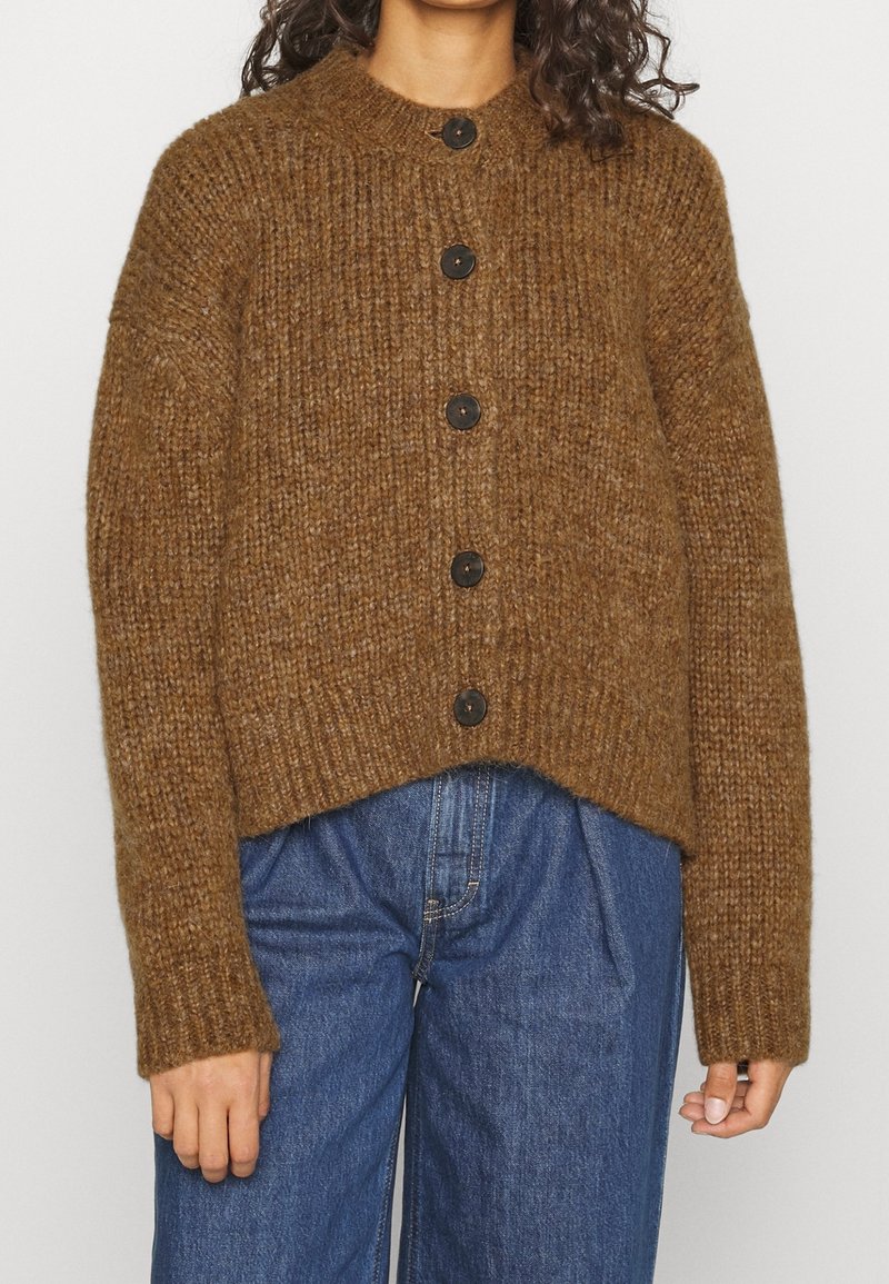 Brun stickad cardigan med rund hals, prydd med stora svarta knappar och en cropped design. Texturerad, varm garn med långa ärmar.