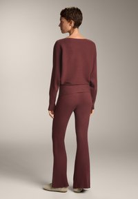 Maroonski pleteni pulover in flared hlače z rebrasto teksturo. Pulover ima širok izrez, hlače pa se ponašajo s prilegajočim pasom.