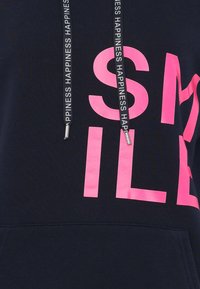 Felpa nera con cappuccio caratterizzata da un grande testo rosa che recita "SORRIDI". Include lacci con la scritta "FELICITÀ" stampata su di essi. Tessuto morbido.