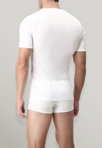 T-shirt bianco in cotone con scollo rotondo e pantaloni corti aderenti coordinati, texture liscia, maniche corte e design minimalista su sfondo grigio.