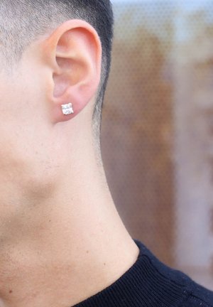 Square silver stud earring on the lobe of a short-haired ear, showcasing a clear, faceted surface with polished edges.