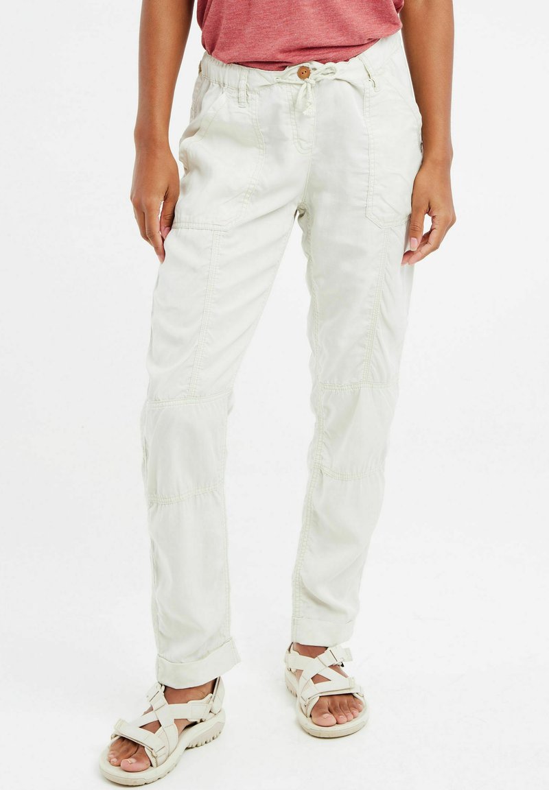 Pantaloni cargo elasticizzati di colore chiaro, a forma affusolata, con cuciture visibili, chiusura con bottone e tasche laterali. Indossati con sandali a striscia regolabile.
