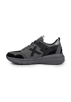 Zapatilla deportiva gris con acentos negros, malla transpirable, gamuza texturizada y una suela moteada. Presenta cordones redondos y un collar acolchado.