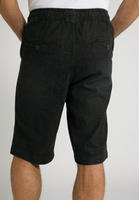 Pantalones cortos de mezclilla negros con una cinturilla elástica, dos bolsillos traseros con cierres de botón y un corte recto. Presenta una textura suave.