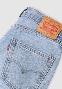 Ανοιχτό μπλε τζιν παντελόνι Levi's διπλωμένο ώστε να φαίνεται η πίσω τσέπη με τη χαρακτηριστική ραφή arcuate, την κόκκινη ετικέτα και την ταμπέλα από δέρμα χρώματος ταμπά.