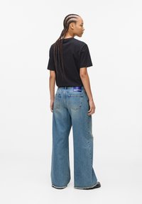 Black short-sleeve t-shirt paired with light blue wide-leg jeans, featuring a distressed hem and a visible tag on the waistband.