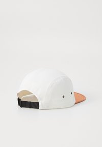 White baseball cap with a curved orange brim, textured fabric, black adjustable strap at the back, and ventilation eyelets on the sides.