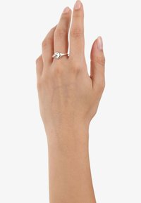 Anello in argento esposto su una mano, caratterizzato da una forma a goccia con pietre trasparenti e una finitura lucida. Due pietre accentuano il design.