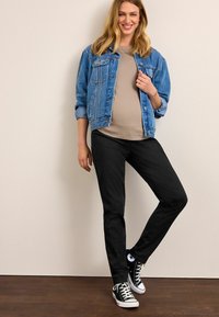 Modrá džínsová bunda s voľným strihom, béžový top, čierne slim-fit nohavice a čierne nízke tenisky. Hladká textúra a ležérny dizajn.