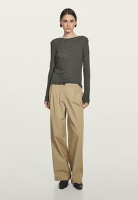 Szary wełniany sweter z dekoltem w łódkę, w połączeniu z beżowymi spodniami o szerokich nogawkach z kantem i zapięciem na jeden guzik. Czarne buty.