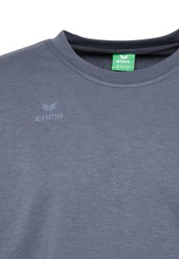 Maglietta grigia a maniche corte realizzata in tessuto leggero. Presenta un colletto rotondo, un discreto logo sul petto e un'etichetta verde.
