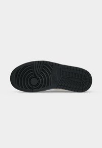 Μαύρη λαστιχένια σόλα παπουτσιού Nike με κυκλικά και πλέγμα μοτίβα πέλματος και το λογότυπο Nike κοντά στο κέντρο σε απλό γκρι φόντο.